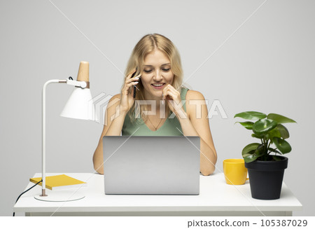 Blonde business woman working with a laptop at office while talking on smartphone with a bussnes partner, colegue, friends. Blonde business woman working with a laptop at office while talking on smartphone with a bussnes partner, colegue, friends. 105387029