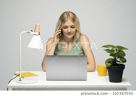 Portrait of shiny positive lady dressed green t-shirt and sitting at the table with laptop talking with a phone with a business partner, colleague, friends. Portrait of shiny positive lady dressed green t-shirt and sitting at the table with laptop talking with a phone with a business partner, colleague, friends. 105387030