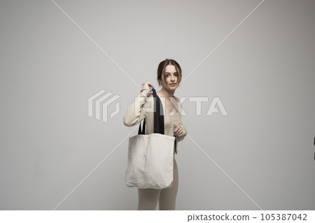 Cheerful millennial woman with a white eco bag standing over white studio background. Lady holding shopper handbag. Fashion and ecology concept, Selective Focus. No more plastic. Cheerful millennial woman with a white eco bag standing over white studio background. Lady holding shopper handbag. Fashion and ecology concept, Selective Focus. No more plastic. 105387042