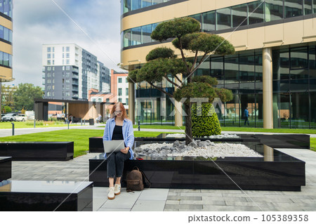 Portrait of successful professional businesswoman in smart casual using laptop outdoors in urban park background. Business people concept. 105389358