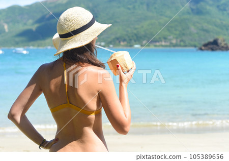 Young woman in yellow swimsuit drinking coconut on a sandy beach 105389656