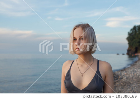 Beautiful short-haired blonde woman standing on the background of blue sea and cloudy sky 105390169