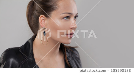 Gold earring with black stone on ear of beautiful model on grey banner background Gold earring with black stone on ear of beautiful model on grey banner background 105390188