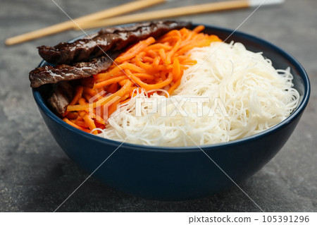 Tasty cooked rice noodles with meat and carrot on grey table Tasty cooked rice noodles with meat and carrot on grey table 105391296