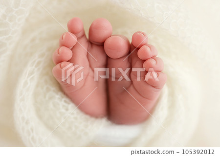 The tiny foot of a newborn baby. Soft feet of a new born in a white wool blanket. Close up of toes, heels and feet of a newborn. Knitted white heart in the legs of a baby. Macro photography. 105392012