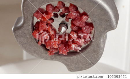 Closeup of minced meat flowing out of meat grinder. Cooking at home, kitchen appliance, healthy nutrition, hamburger ingredients. 105393451