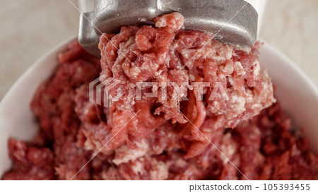 Closeup of minced meat coming out of electric grinder and falling in bowl. Cooking at home, kitchen appliance, healthy nutrition, hamburger ingredients. 105393455