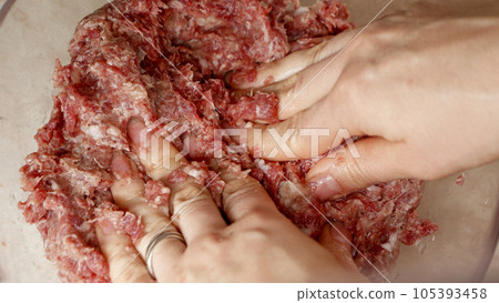 Closeup of female hand beating and mixing minced meat with spices. Cooking at home, kitchen appliance, healthy nutrition, hamburger ingredients. 105393458