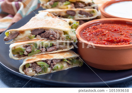 Fajita quesadilla with pieces of beef steak, green bell pepper, onion and cheese, on a plate Fajita quesadilla with pieces of beef steak, green bell pepper, onion and cheese, on a plate 105393638