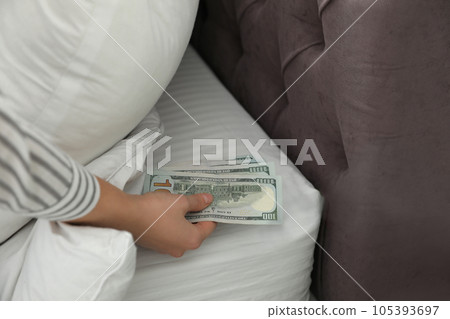 Woman hiding dollar banknotes under pillow in bedroom, closeup. Money savings Woman hiding dollar banknotes under pillow in bedroom, closeup. Money savings 105393697
