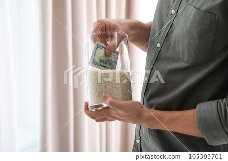 Man hiding money in jar of rice indoors, closeup. Financial savings 105393701