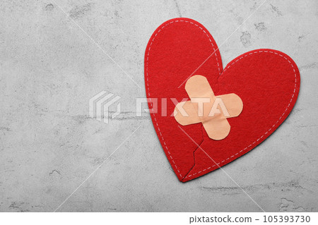 Red fabric heart with sticking plasters on light grey stone table, top view. Space for text 105393730