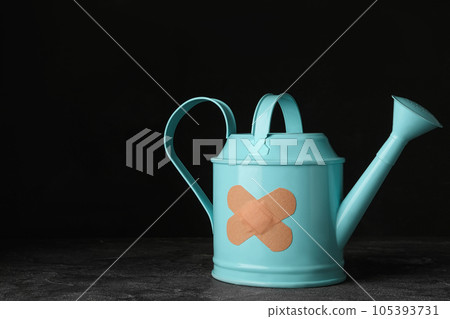 Light blue watering can with sticking plasters on grey stone table. Space for text 105393731