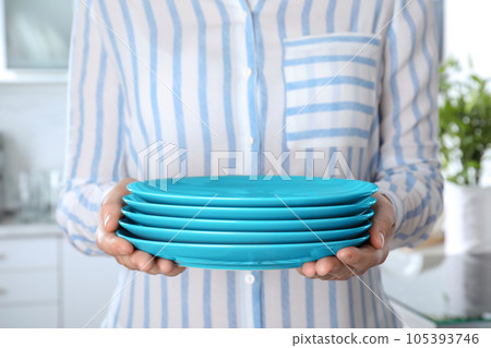 Woman holding stack of clean blue plates in kitchen, closeup Woman holding stack of clean blue plates in kitchen, closeup 105393746