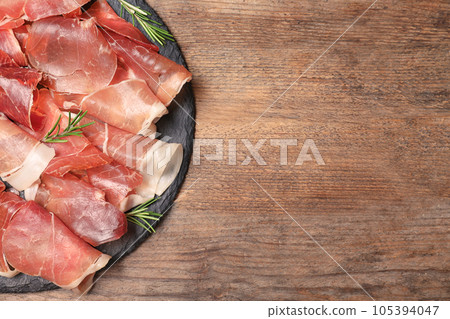 Pile of tasty prosciutto on wooden table, top view. Space for text 105394047