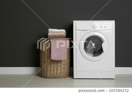 Modern washing machine and laundry basket near black wall Modern washing machine and laundry basket near black wall 105394232