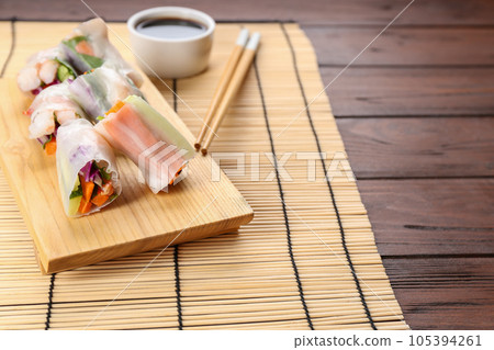 Delicious rolls wrapped in rice paper served on wooden table Delicious rolls wrapped in rice paper served on wooden table 105394261