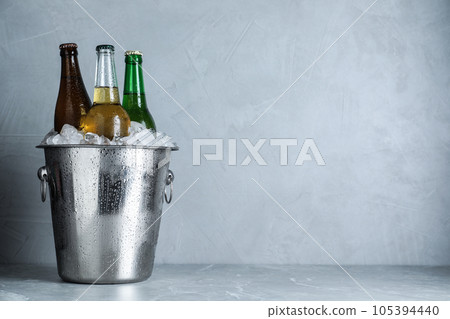 Beer in metal bucket with ice on marble table. Space for text Beer in metal bucket with ice on marble table. Space for text 105394440
