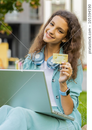 Girl using credit bank card and laptop, transferring money, purchases online shopping in city park Girl using credit bank card and laptop, transferring money, purchases online shopping in city park 105394590