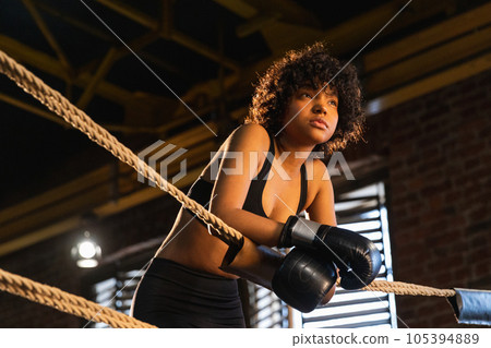 Woman fighter girl power. African american woman fighter with boxing gloves standing on boxing ring leaning on ropes waiting and resting. Strong powerful girl. Strength fit body workout training 105394889