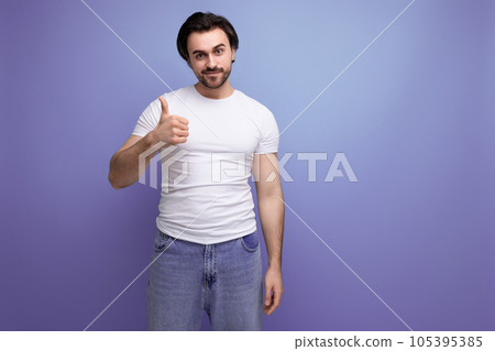 confident young brutal brunette man in a white t-shirt and jeans shows class with his hand 105395385