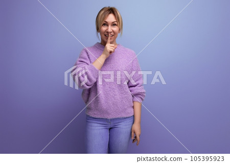 cute blond woman in lavender sweater showing silence gesture on purple background with copy space 105395923