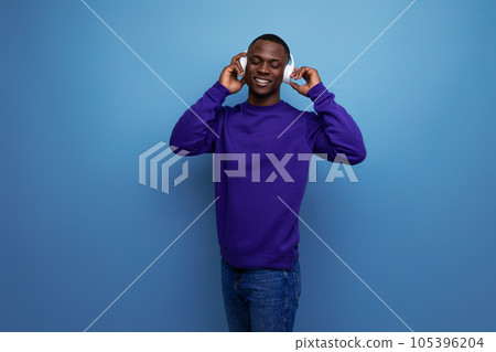 handsome young american man in blue sweatshirt listening to music in wireless bluetooth headphones 105396204