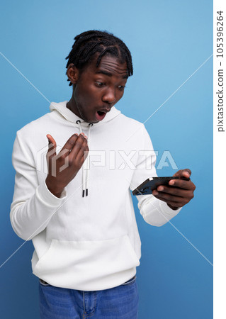 surprised young african guy in a white sweatshirt understands the smartphone surprised young african guy in a white sweatshirt understands the smartphone 105396264