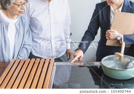 一位女商人(IH 烹飪加熱器)在住宅展覽/樣板間向顧客解釋 一位女商人(IH 烹飪加熱器)在住宅展覽/樣板間向顧客解釋 105400744