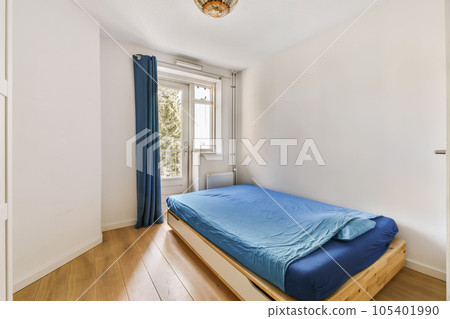 a bedroom with wood flooring and blue sheets on the bed in front of the window looking out onto the street 105401990