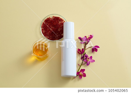 On the beige background, a white cosmetic bottle unbranded decorated with fresh crocus sativus, stigmas saffron and a beaker filled yellow liquid. Cosmetic mockup for advertising and design 105402065
