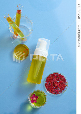 Mockup scene with a pump bottle unbranded displayed on blue background with fresh ingredient: stigmas saffron, yellow essence and flower. Space for design packaging Mockup scene with a pump bottle unbranded displayed on blue background with fresh ingredient: stigmas saffron, yellow essence and flower. Space for design packaging 105402073