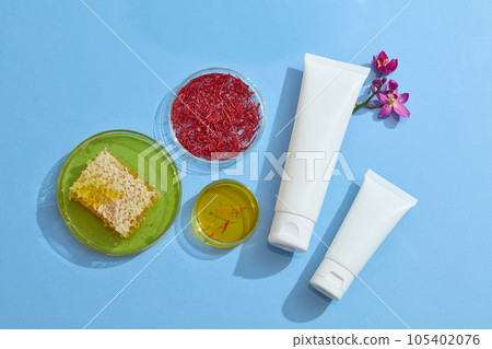 Empty bottle mockup for cosmetic decorated with natural ingredient: stigmas saffron, beeswax and fresh crocus sativus on the blue background. Saffron may have antioxidant and anticancer benefit 105402076