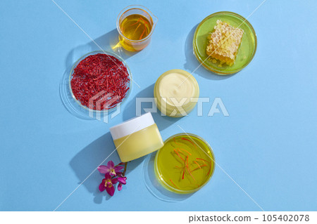Against the blue background, yellow jars unlabeled decorated with petri dishes containing stigmas saffron, yellow essence and beeswax. Mockup for advertising cosmetic extracted from saffron 105402078