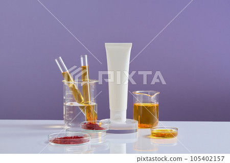White tube standing on a podium in round-shaped, glassware containing saffron and yellow fluid surrounded. Mockup of skin care cosmetic tube of beauty facial 105402157