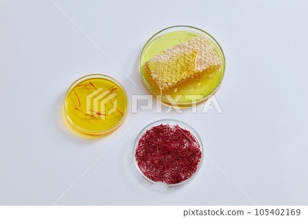 White background featured three glass petri dishes containing honeycomb, saffron and liquid in yellow color. Saffron is rich in antioxidants 105402169