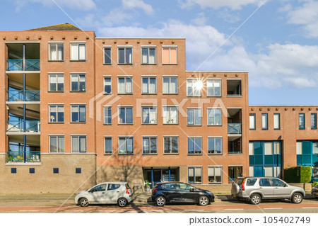 an apartment building with cars parked on the street in front of it and blue sky above, as seen from across the street an apartment building with cars parked on the street in front of it and blue sky above, as seen from across the street 105402749