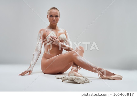 Nude ballerina in gypsum sitting on the floor of studio 105403917