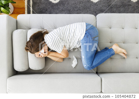 Frustrated woman covering face and crying, lying on sofa at home alone 105404872