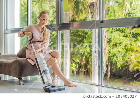 Young pregnant woman enjoys cleaning her house. Easy cleaning with a wireless vacuum cleaner. Pregnant woman cleaning floor with handheld vacuum cleaner. Modern easy cleaning Young pregnant woman enjoys cleaning her house. Easy cleaning with a wireless vacuum cleaner. Pregnant woman cleaning floor with handheld vacuum cleaner. Modern easy cleaning 105405027
