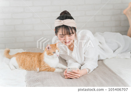 與寵物貓玩耍的亞洲女性在家裡的臥室裡用智能手機拍照 與寵物貓玩耍的亞洲女性在家裡的臥室裡用智能手機拍照 105406707