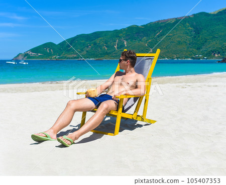 Young happy man drinks coconut juice sitting on deck chair on a south china sea beach in vietnam 105407353