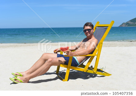 Young man eating watermelon on a white sandy beach in Vietnam Young man eating watermelon on a white sandy beach in Vietnam 105407356