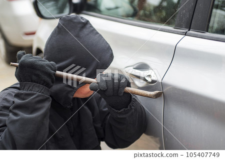 Robber man in black hoodie jacket using crowbar to break lock and steal vehicle Robber man in black hoodie jacket using crowbar to break lock and steal vehicle 105407749