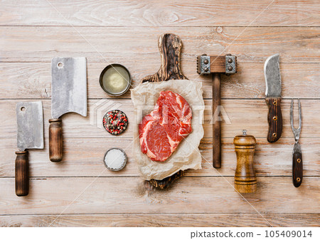 Raw beef rib eye with meat utensils set on wooden background 105409014