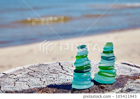 Two Zen pyramids of blue and green glass stones on wooden surface against background of coastal sea waves 105411943