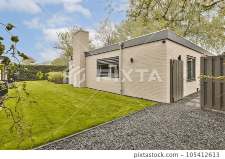 a small house in the middle of a green lawn with trees and bushes behind it on a blue sky day 105412613