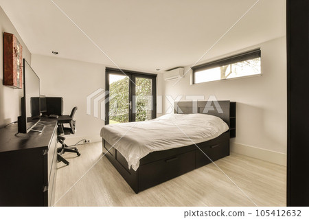 a bedroom with a bed, desk and television on the wall in front of the bed is white wood flooring a bedroom with a bed, desk and television on the wall in front of the bed is white wood flooring 105412632
