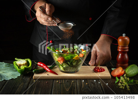 The chef adds flavoring to the vegetable salad. Vegetarian food by hands of the cook in the kitchen. Menu idea for a hotel or restaurant The chef adds flavoring to the vegetable salad. Vegetarian food by hands of the cook in the kitchen. Menu idea for a hotel or restaurant 105413498