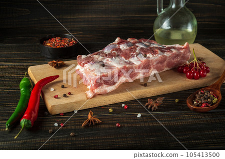 Fresh raw chopped pork ribs on a kitchen cutting board with spices and hot peppers. Cooking delicious food at home. Fresh raw chopped pork ribs on a kitchen cutting board with spices and hot peppers. Cooking delicious food at home. 105413500